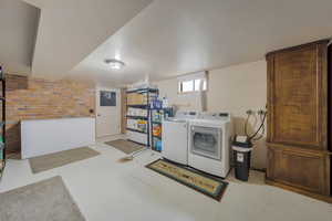 Clothes washing area with independent washer and dryer, electric panel, and brick wall