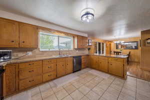 Kitchen featuring stainless steel microwave, dishwashing machine, a sink, brown cabinetry, and backsplash