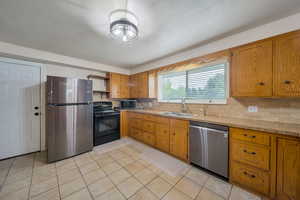Kitchen with stainless steel appliances, a sink, open shelves, brown cabinetry, and tasteful backsplash
