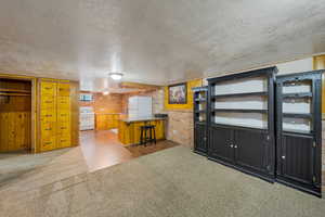 Kitchen featuring white appliances, a textured ceiling, carpet floors, and brick wall