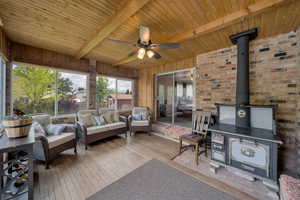 Living area featuring a wood stove, beam ceiling, a ceiling fan, wood ceiling, and hardwood / wood-style flooring