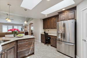 Kitchen featuring stainless steel fridge, arched walkways, a skylight, dark brown cabinets, and recessed lighting