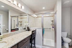 Bathroom featuring toilet, vanity, a shower stall, and recessed lighting