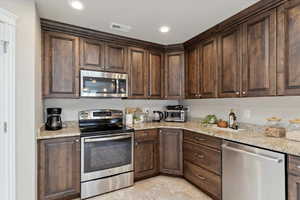 Kitchen featuring appliances with stainless steel finishes, dark brown cabinets, light tile patterned flooring, light stone counters, and recessed lighting