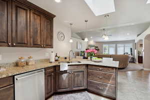 Kitchen featuring stainless steel dishwasher, a sink, a peninsula, dark brown cabinetry, and open floor plan