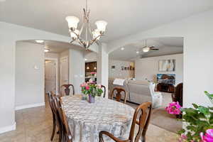 Dining room featuring arched walkways, a ceiling fan, light tile patterned flooring, a chandelier, and baseboards