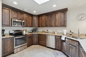 Kitchen with stainless steel appliances, a sink, light tile patterned floors, dark brown cabinets, and recessed lighting