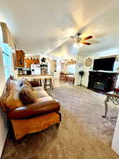 Living room with a textured ceiling, ceiling fan, a glass covered fireplace, and carpet