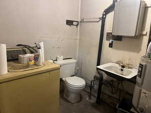 Bathroom with unfinished concrete flooring, a sink, toilet, and water heater