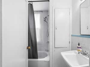 Full bath with a sink, tile walls, and shower / tub combo with curtain
