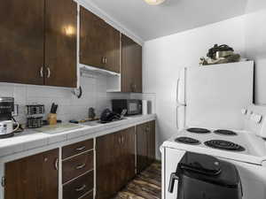 Kitchen featuring white appliances, tile countertops, dark brown cabinetS