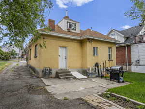 Back of property featuring entry steps, stucco siding, a chimney, and fence