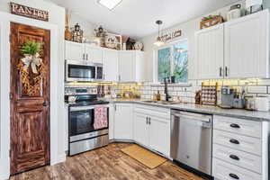 Kitchen with stainless steel appliances, lofted ceiling, decorative backsplash, a sink, and white cabinetry