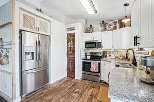 Kitchen featuring stainless steel appliances, a sink, dark wood-type flooring, decorative backsplash, and light stone counters