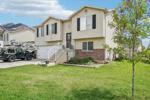 Split foyer home featuring brick siding, concrete driveway, a front yard, and a garage