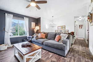 Living room with dark wood-type flooring, baseboards, a chandelier, a textured ceiling, and wood walls