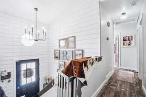 Interior space featuring a chandelier, dark wood finished floors, wood walls, baseboards, and a textured ceiling