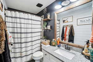 Bathroom with toilet, vanity, and a shower with shower curtain