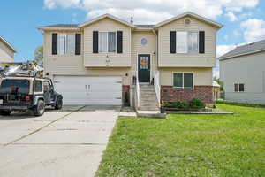 Raised ranch with brick siding, a garage, a front lawn, and driveway
