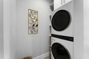 Clothes washing area with stacked washer / drying machine, baseboards, and wood finished floors