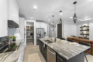 Kitchen with stainless steel appliances, wall chimney exhaust hood, a center island with sink, white cabinetry, and a breakfast bar area