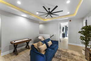 Sitting room featuring a raised ceiling, recessed lighting, ceiling fan, light wood finished floors, and baseboards