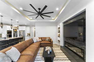 Living area featuring ceiling fan, recessed lighting, a tray ceiling, a fireplace, and baseboards