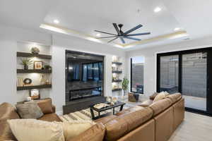 Living area featuring a tile fireplace, a tray ceiling, a ceiling fan, recessed lighting, and light wood-style flooring