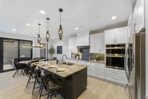 Kitchen with a sink, appliances with stainless steel finishes, light stone counters, decorative backsplash, and white cabinetry