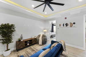 Living room featuring recessed lighting, a ceiling fan, baseboards, light wood finished floors, and a tray ceiling