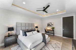 Bedroom featuring a tray ceiling, baseboards, light wood-type flooring, recessed lighting, and ceiling fan