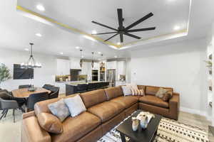 Living area featuring a raised ceiling, a ceiling fan, recessed lighting, light wood-type flooring, and a chandelier
