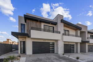 View of front of property featuring an attached garage, driveway, stucco siding, a balcony, and fence