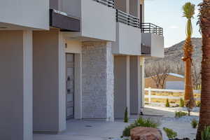 Entrance to property with a balcony, stone siding, stucco siding, a mountain view, and fence