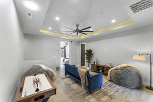 Living room with a tray ceiling, a ceiling fan, wood finished floors, recessed lighting, and baseboards