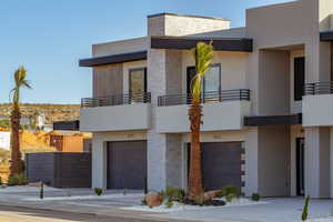View of front facade with a balcony, an attached garage, stone siding, and stucco siding