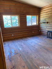 Unfurnished living room featuring rustic walls, hardwood / wood-style flooring, and vaulted ceiling