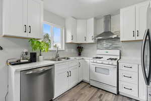 Kitchen featuring white gas stove, dishwasher, exhaust hood, a sink, and white cabinetry