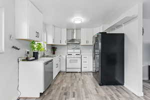 Kitchen with appliances with stainless steel finishes, wall chimney exhaust hood, a sink, light wood-style floors, and light countertops