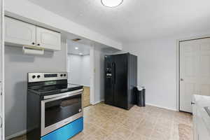 Kitchen featuring stainless steel electric range, black fridge with ice dispenser, white cabinets, light countertops, and baseboards