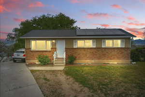 View of front of house featuring brick siding, a front lawn, roof mounted solar panels, a shingled roof, and driveway