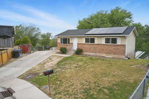 Single story home featuring brick siding, solar panels, driveway, and roof with shingles