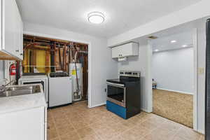 Kitchen featuring stainless steel range with electric cooktop, water heater, washer and dryer, white cabinetry, and a sink