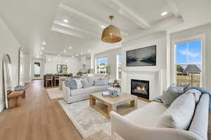 Living area with beamed ceiling, a glass covered fireplace, recessed lighting, and light wood-style flooring