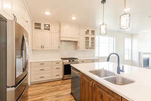 Kitchen with stainless steel appliances, light countertops, a sink, light wood finished floors, and hanging light fixtures