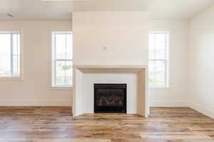 Unfurnished living room with wood finished floors, baseboards, and a glass covered fireplace