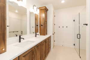 Bathroom featuring a shower stall, recessed lighting, double vanity, and baseboards