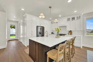 Kitchen featuring dark brown cabinets, stainless steel refrigerator with ice dispenser, white cabinets, an island with sink, and a kitchen breakfast bar