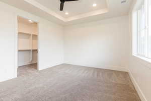 Unfurnished bedroom with carpet floors, a walk in closet, recessed lighting, a raised ceiling, and baseboards