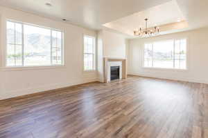 Unfurnished living room featuring a raised ceiling, hardwood / wood-style floors, a chandelier, baseboards, and a glass covered fireplace